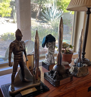 P's three Hugo Awards, his World Fantasy Award, and P&T's Skylark Award, with a corner of our desert-garden back yard in view behind